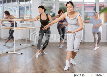 Group of women of different ages are learning various dance and ballet movements in studio 135696873