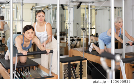 Female pilates trainer helping pilates woman during training Female pilates trainer helping pilates woman during training 135696935