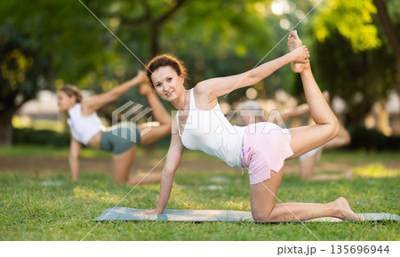 Happy sporty skilled young women going table pose of yoga with group in park at daytime 135696944