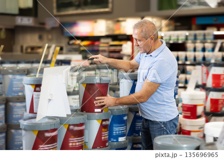 Elderly male shopper carefully selects a can of paint for home renovation 135696965