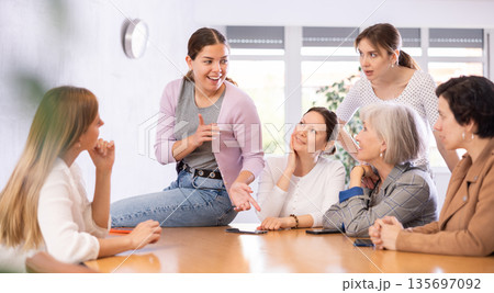 young girl student sits on table near friends and promotes version of solution of educational task 135697092