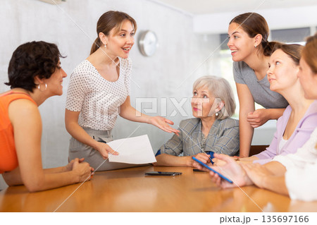 Women discuss documents sitting at table in office 135697166