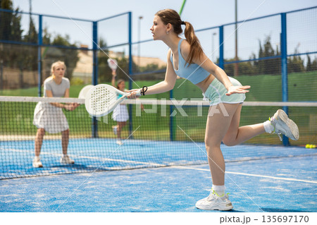 Young woman playing paddle tennis against team of women 135697170