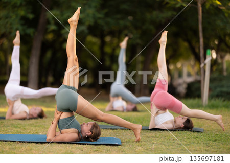 Yoga lesson visitors girls perform Salamba Sarvangasana in park Yoga lesson visitors girls perform Salamba Sarvangasana in park 135697181