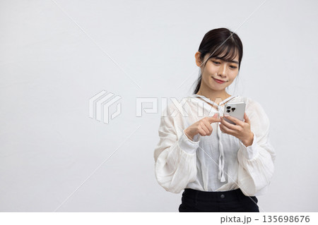 白い背景の前でスマートフォンを操作する笑顔の若い女性 135698676