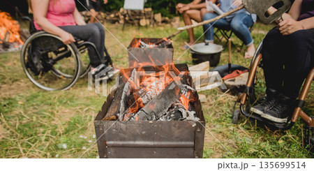 Disabled woman fries meat at the stake in a campsite with friends. Disabled woman fries meat at the stake in a campsite with friends. 135699514