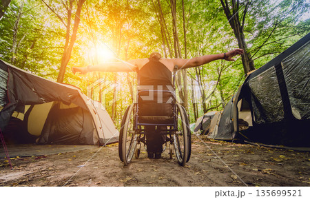 Disabled man resting in a campsite with friends. Wheelchair in the forest  135699521