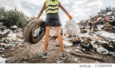 Woman volunteer helps clean the field of plastic garbage and old tires. Woman volunteer helps clean the field of plastic garbage and old tires. 135699594