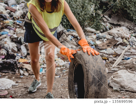 Woman volunteer helps clean the field of plastic garbage and old tires. Woman volunteer helps clean the field of plastic garbage and old tires. 135699596