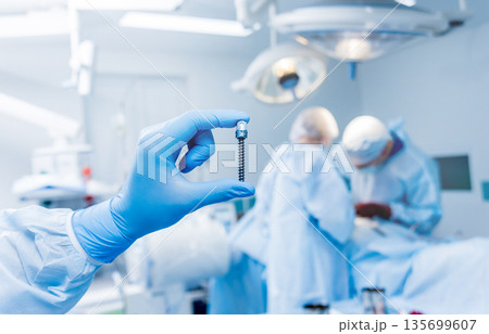 Spinal surgery. Surgeon show polyaxial screw in operating room  135699607