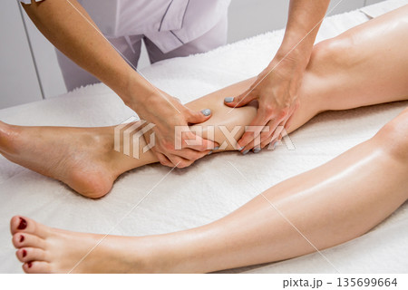 Beautiful young woman enjoying legs massage with oil in spa salon. Cosmetology 135699664