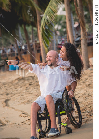 Disabled man in a wheelchair with his wife on the beach. Disabled man in a wheelchair with his wife on the beach. 135699848