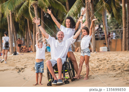 Disabled man in a wheelchair with his family on the beach. Disabled man in a wheelchair with his family on the beach. 135699850