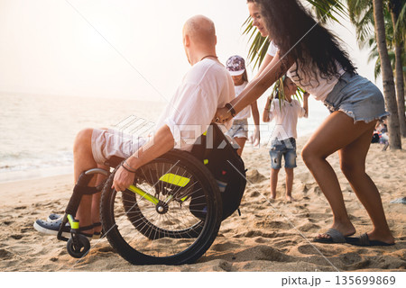 Disabled man in a wheelchair with his wife on the beach. Disabled man in a wheelchair with his wife on the beach. 135699869