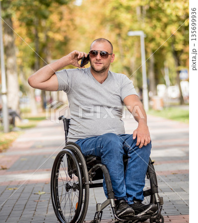Handicapped man in wheelchair at the park alley use a smartphone 135699936