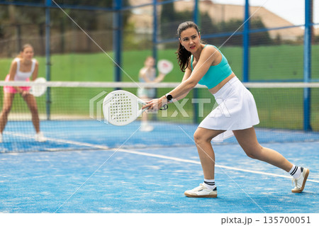 Adult woman plays paddle tennis against team of women 135700051