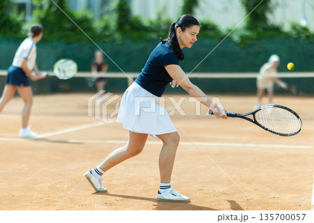 Adult woman playing doubles tennis on court Adult woman playing doubles tennis on court 135700057