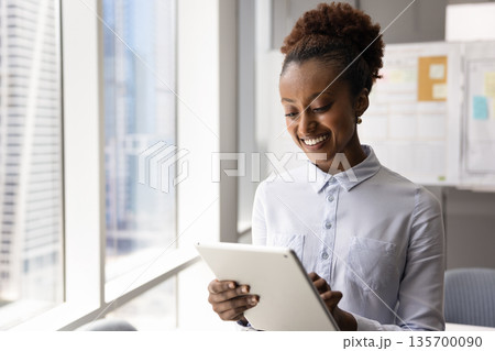 Smiling African businesswoman working online using modern tablet device Smiling African businesswoman working online using modern tablet device 135700090