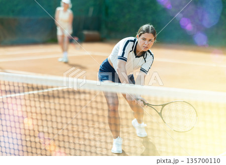 Girl plays tennis on open court with opponent 135700110