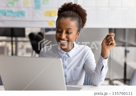 Happy African woman reading great news on laptop 135700111