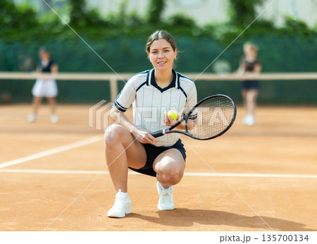 Woman in sportswear against backdrop of outdoor tennis court. 135700134