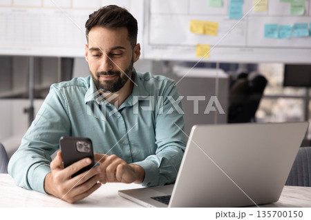 Businessman sit at desk with laptop using his modern smartphone 135700150