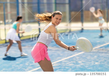 Young woman playing paddle tennis against team of women 135700151