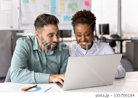 Two multinational smiling colleagues looking at laptop screen Two multinational smiling colleagues looking at laptop screen 135700184