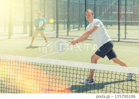 Men play padel on an outdoor tennis court. Hitting the ball with racket Men play padel on an outdoor tennis court. Hitting the ball with racket 135700186