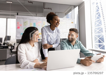 Group of laughing teammates engaged in positive communication in workplace Group of laughing teammates engaged in positive communication in workplace 135700207