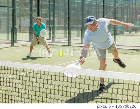 Two adult men playing doubles padel Two adult men playing doubles padel 135700226