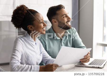 Teammates looking into distance with contented smile in workplace 135700228