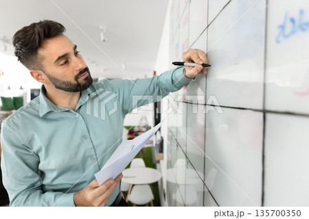 Focused man engaged with large, gridded whiteboard Focused man engaged with large, gridded whiteboard 135700350