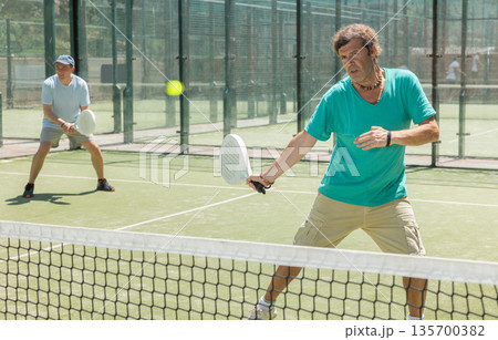 Two adult men playing doubles padel 135700382