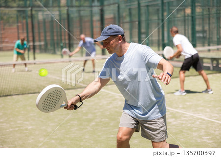 Four men practice playing padel on an outdoor court 135700397
