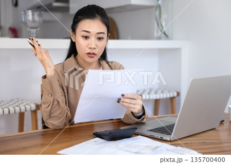 Woman review data in documents with concerned expression Woman review data in documents with concerned expression 135700400