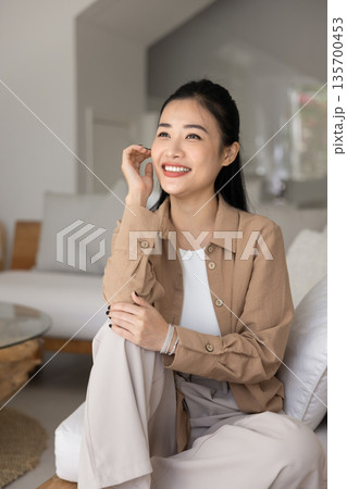 Woman daydreaming seated on cozy sofa in modern living room Woman daydreaming seated on cozy sofa in modern living room 135700453