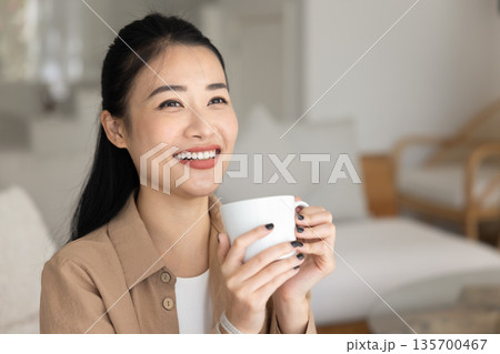 Closeup of happy Asian woman holding mug with favourite beverage 135700467