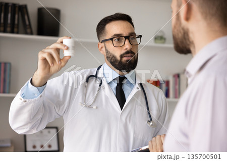 Portrait confident doctor presenting new prescribed medication to male patient 135700501