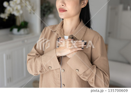 Woman praying touches her chest with both palms pressed together Woman praying touches her chest with both palms pressed together 135700609