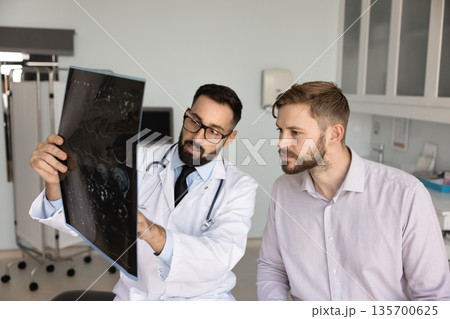 Serious Hispanic medical practitioner explaining X-ray to young male patient Serious Hispanic medical practitioner explaining X-ray to young male patient 135700625