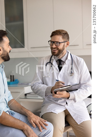 Positive young physician man asking patient about healthcare Positive young physician man asking patient about healthcare 135700662
