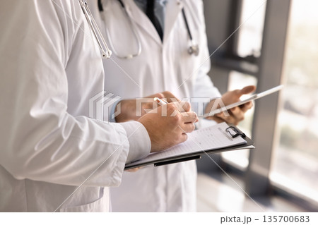 Cropped shot of male doctor consulting colleague, writing notes Cropped shot of male doctor consulting colleague, writing notes 135700683