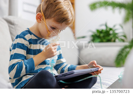 Child Using Nebulizer While Engaged with Tablet at Home 135700723