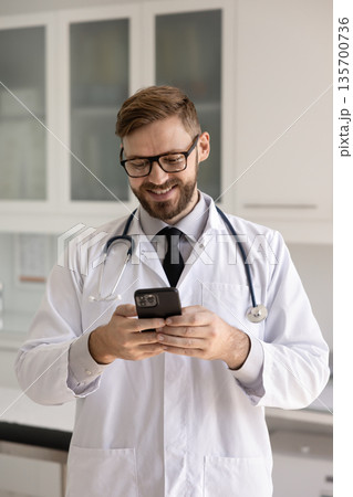 Positive doctor in glasses and stethoscope typing on mobile phone Positive doctor in glasses and stethoscope typing on mobile phone 135700736