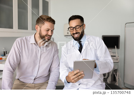 Cheerful young Hispanic doctor showing medical report to patient 135700748