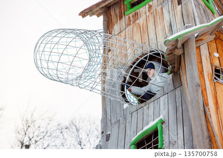 Child Playing in Wooden Treehouse with Metal Tunnel in Winter Child Playing in Wooden Treehouse with Metal Tunnel in Winter 135700758