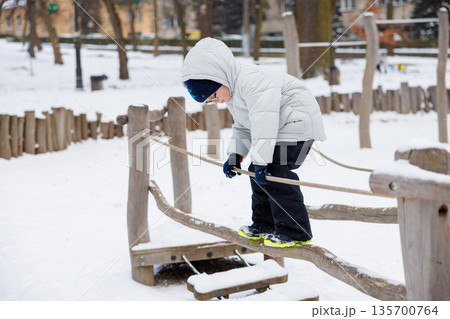 Child Balancing on Rope Bridge in Snowy Playground 135700764