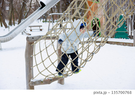 Child Climbing Rope Net in Snowy Playground Winter Adventure Child Climbing Rope Net in Snowy Playground Winter Adventure 135700768