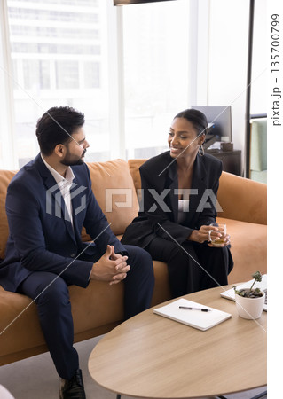 Two diverse business professionals have casual conversation sitting on sofa Two diverse business professionals have casual conversation sitting on sofa 135700799
